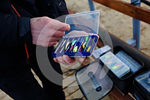 Organizer with a set of artificial lures for fishing in the hands of a fisherman.