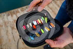 Organizer with a set of artificial lures for fishing in the hands of a fisherman.