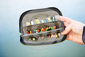 Organizer with a set of artificial lures for fishing in the hands of a fisherman.