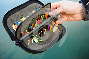 Organizer with a set of artificial lures for fishing in the hands of a fisherman.