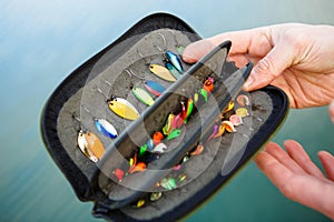 Organizer with a set of artificial lures for fishing in the hands of a fisherman.