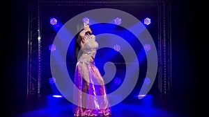 Oriental belly dancer is dancing and demonstrating the flexibility and attractiveness of her body. Blue background neon