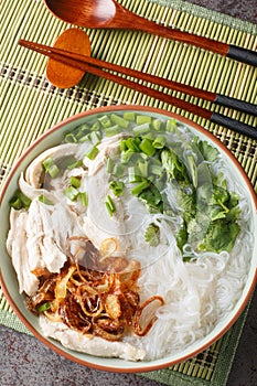 Oriental clear chicken soup with noodles, fried onions, green onions and cilantro close-up in a bowl on the table. Vertical top