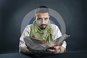 Oriental man in traditional national Arabic dress, with interest reads the old big book