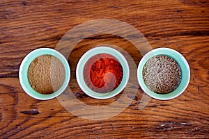 Oriental spices cumin, ground zira and red pepper paprika in bowls on a wooden oak table. Flat lay. Soft selective focus