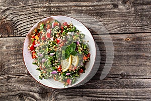 Oriental tabbouleh salad with couscous, vegetables and herbs in a brown bowl on wooden background. banner, catering menu recipe