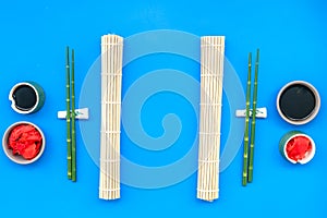 Oriental table set up with bamboo sticks for sushi and maki, soy sauce on blue background top view