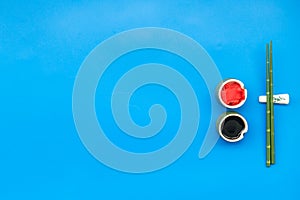 Oriental table set up with bamboo sticks for sushi and maki, soy sauce on blue background top view space for text