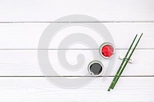Oriental table set up with bamboo sticks for sushi and maki, soy sauce white wooden background top view space for text