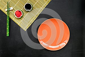 Oriental table set up with plate and bamboo sticks for sushi and maki on black background top view space for text