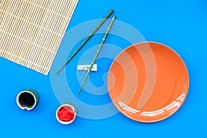 Oriental table set up with plate and bamboo sticks for sushi and maki on blue background top view space for text