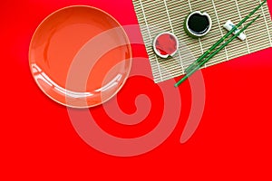 Oriental table set up with plate and bamboo sticks for sushi and maki on red background top view space for text