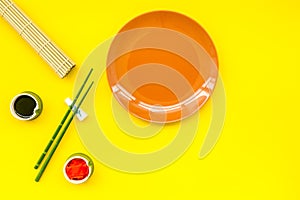 Oriental table set up with plate and bamboo sticks for sushi and maki on yellow background top view space for text