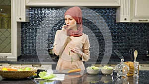 Oriental woman stands at kitchen table and eats greens