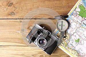 An orientation compass, an old camera and a geographic map rest on a wooden table with copy space for your text