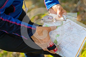 Orienteering athlete running through a summer forest with a map and compass.