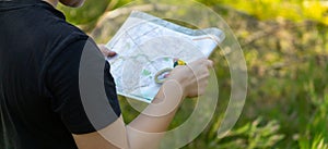 Orienteering athlete running through a summer forest with a map and compass.