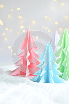 Origami 3D Xmas tree from paper on white background and bokeh lights. Merry Christmas and New Year card. Paper art style. Copy spa