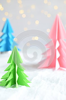 Origami 3D Xmas tree from paper on white background and bokeh lights. Merry Christmas and New Year card. Paper art style. Copy spa