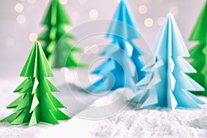 Origami 3D Xmas tree from paper on white background and bokeh lights. Merry Christmas and New Year card. Paper art style. Copy spa