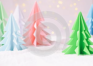 Origami 3D Xmas tree from paper on white background and bokeh lights. Merry Christmas and New Year card. Paper art style. Copy spa