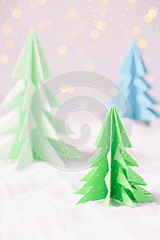 Origami 3D Xmas tree from paper on white background and bokeh lights. Merry Christmas and New Year card. Paper art style. Copy spa