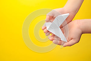 Origami art. Child holding paper bird on yellow background, top view. Space for text