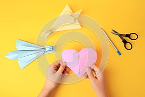 Origami art. Child holding paper figure on yellow background, closeup and top view