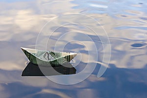 Origami boat built of one hundred dollar bill. paper boat from a hundred dollar bill in blue water. copy space. Concept: