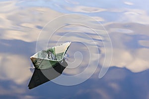 Origami boat built of one hundred dollar bill. paper boat from a hundred dollar bill in blue water. copy space. Concept: