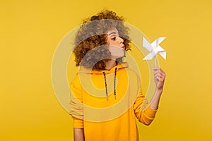 Origami hand mill. Portrait of carefree childish curly-haired woman in hoodie blowing at paper windmill