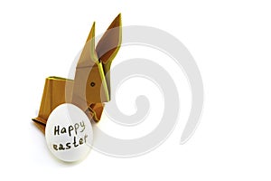 Origami rabbit from orange colored paper. Easter bunny and white chicken egg with the inscription Happy Easter on a white