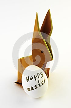 Origami rabbit from orange colored paper. Easter bunny and white chicken egg with the inscription Happy Easter on a white