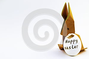 Origami rabbit from orange colored paper. Easter bunny and white with a chopped egg shell with an inscription Happy Easter on a