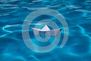 Origami ship. Paper boat on the sea background. Origami paper boat sailing on water causing waves and ripples.