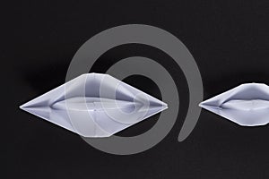 Origami ships of white paper on black background swim one by one. Business concept. small boat sails after large.