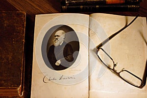 The origin of species by Charles Darwin opened on first page with glasses on the second page.