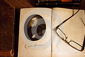 The origin of species by Charles Darwin opened on first page with glasses on the second page. photo