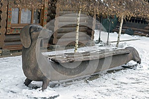 An original bench in a winter park in the form of a dachshund dog