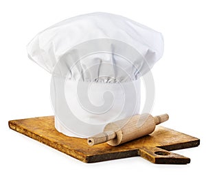 Original cooks cap with wooden rolling-pin on a wooden cutting board.