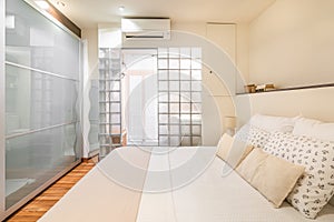 Original design of bright small bedroom with glass wall in the bathroom and glass rack. Concept of an unusual interior