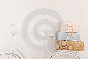 Original festive decor. White bicycle stands against background of white brick wall in back seat is pile of gift boxes. Wrapped in