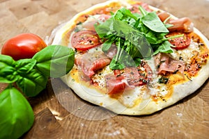 Original Italian Pizza con Prosciutto e Rucola on brown wood background. Pizza with Prosciutto and arugula close up