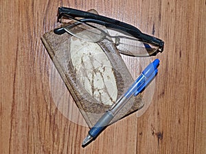 Original leather notebook, ballpoint pen and glasses on a wooden table surface. Closeup. Selective focus.