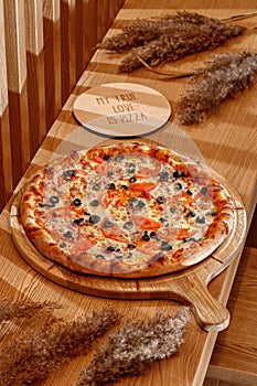 Original neapolitan pizza margherita on a traditional wooden plate , Italy. Pizza with olives.Wooden background, top view