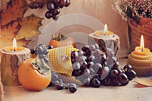 An original still life of Russia with the fire of a wax candle. Candle flame close-up. Still life with blue grapes and persimmons.