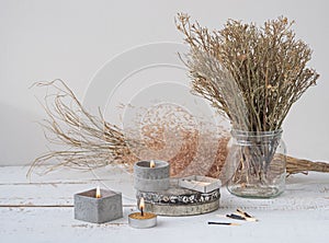 An original still life in the style of wabi-sabi with candles. Candles in concrete candlesticks, restrained dry flowers.