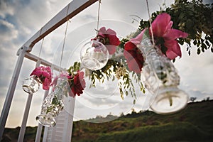 Original wedding floral decoration in form of mini vases and bouquets of flowers hanging from wedding altar, outdoor beach wedding