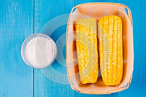 Ð¡orn with salt. Top view. Yellow corn in small basket and salt glass on blue wooden background