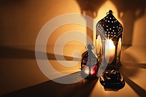 Ornamental Arabic lanterns, burning candles glowing at night. Plate with date fruit on the table. Golden festive